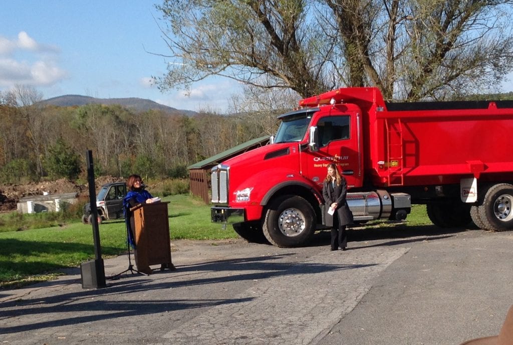 Photo of Dr. Gladys Cruz speaking at a podium next to a red dump truck.